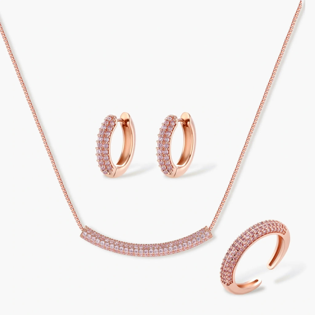 Rose gold pavé zirconia bar necklace, hoop earrings, and open ring set with pink stones on cream background.