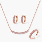Rose gold pavé zirconia bar necklace, hoop earrings, and open ring set with pink stones on cream background.