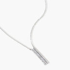 White gold plated necklace with vertical cubic zirconia pendant and matching hoop earrings on neutral background