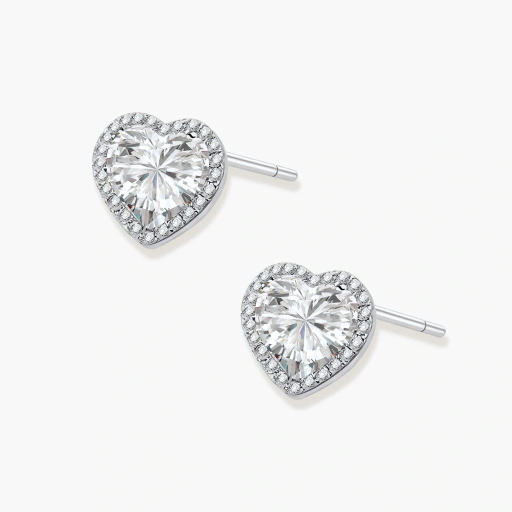 Close-up of heart-shaped moissanite stud earrings in sterling silver halo setting on cream background.
