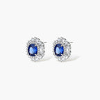 White gold plated jewelry set with blue cubic zirconia centers surrounded by clear crystal halos on cream background.