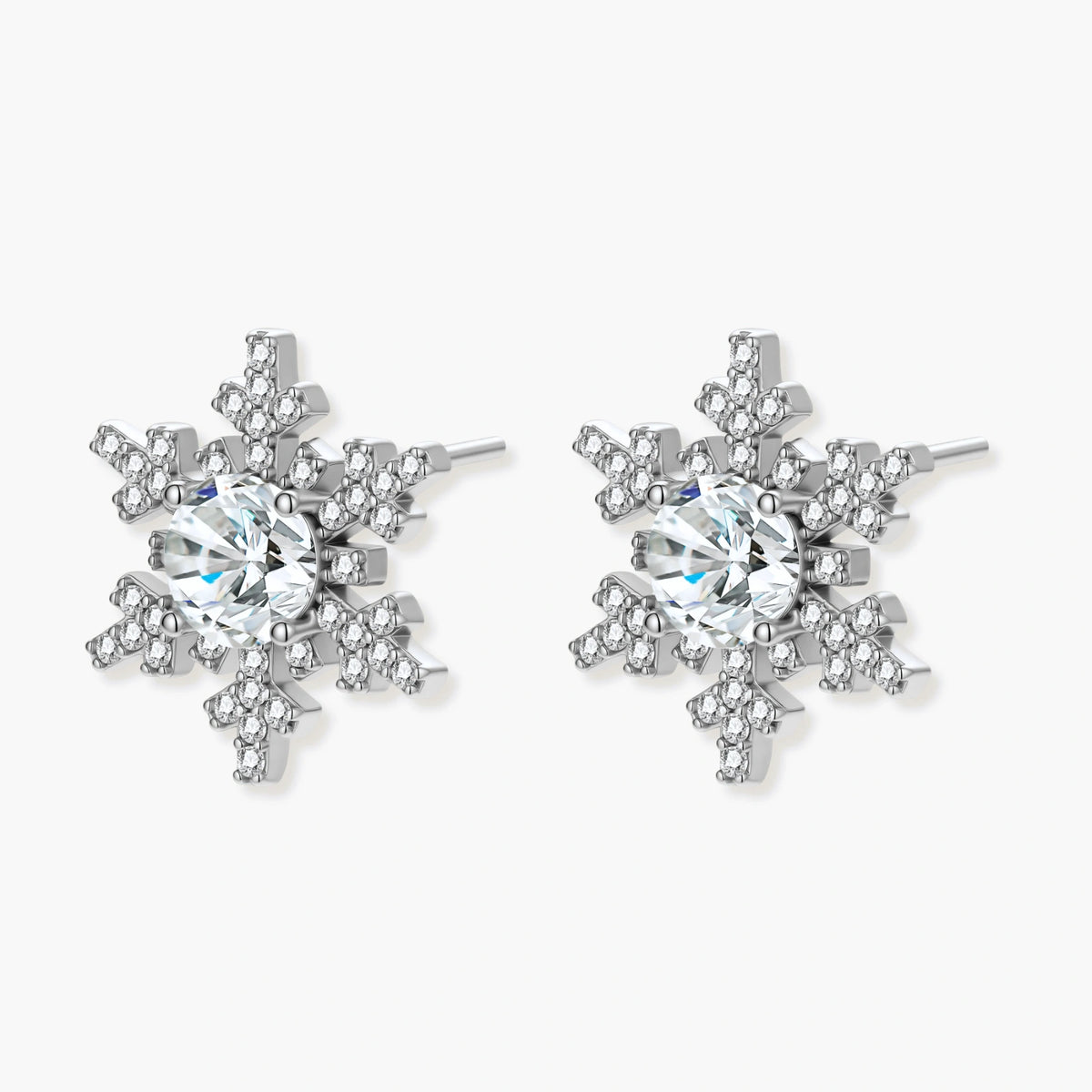 Sterling silver snowflake stud earrings with brilliant moissanite centers and intricate geometric patterns on cream background