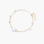 Delicate gold chain bracelet with baroque pearl centerpiece and small freshwater pearls on cream background.