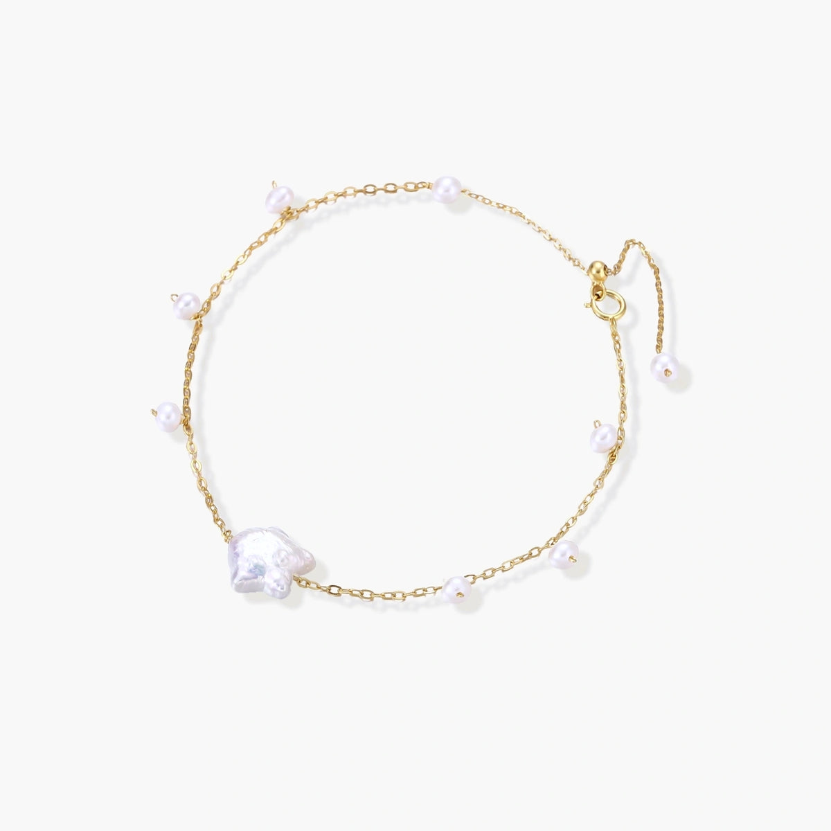Delicate gold chain bracelet with baroque pearl centerpiece and small freshwater pearls on cream background.