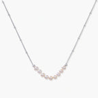 Delicate sterling silver chain necklace with small freshwater pearls arranged in a curved smile arc on cream background.