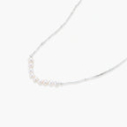 Delicate sterling silver chain necklace with small freshwater pearls arranged in a curved smile arc on cream background.