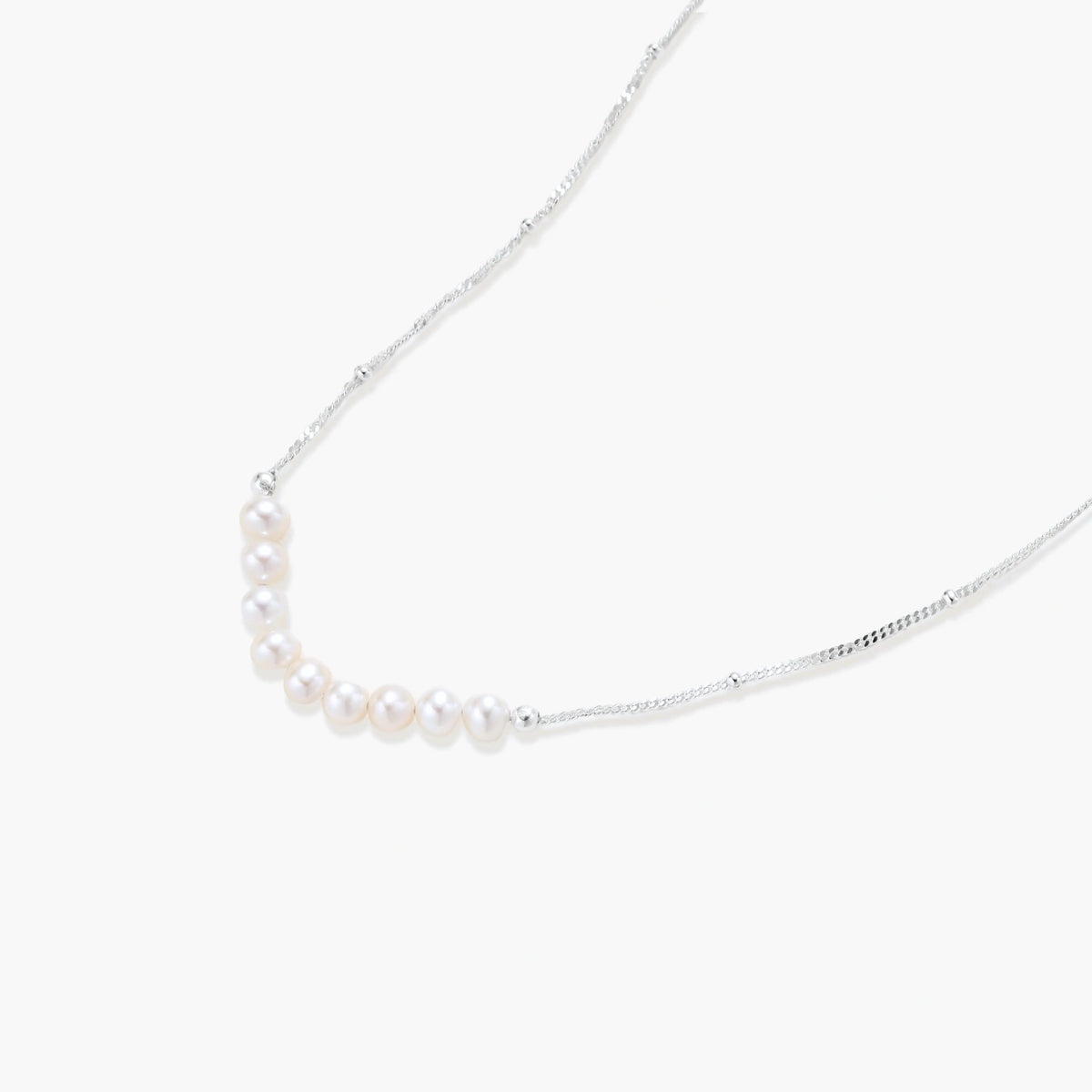 Delicate sterling silver chain necklace with small freshwater pearls arranged in a curved smile arc on cream background.