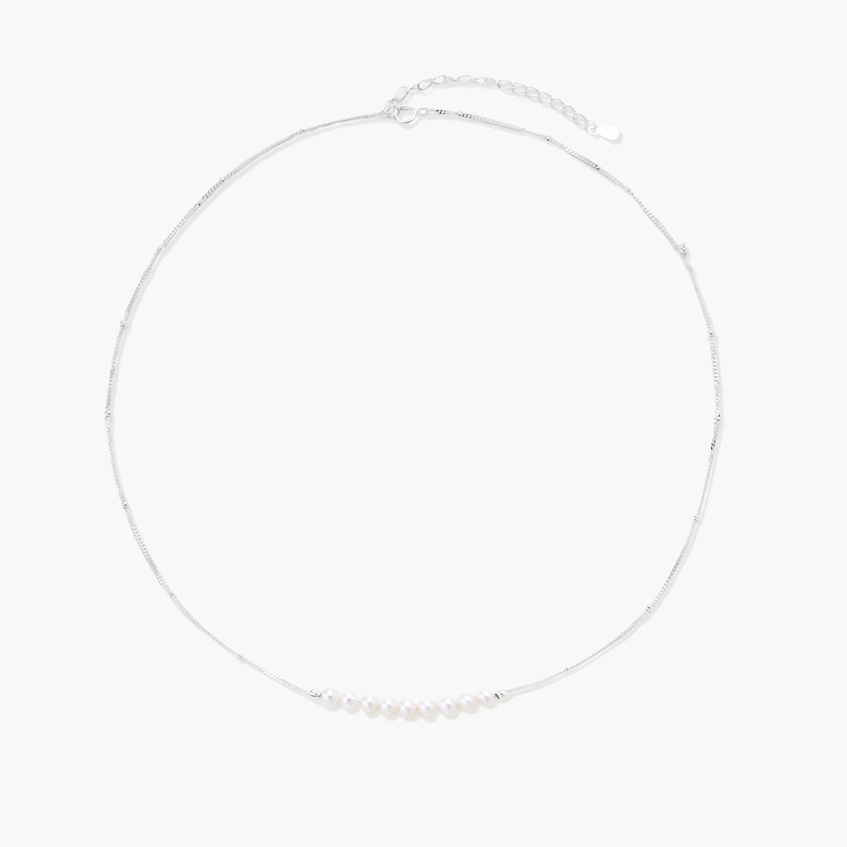 Delicate sterling silver chain necklace with small freshwater pearls arranged in a curved smile arc on cream background.