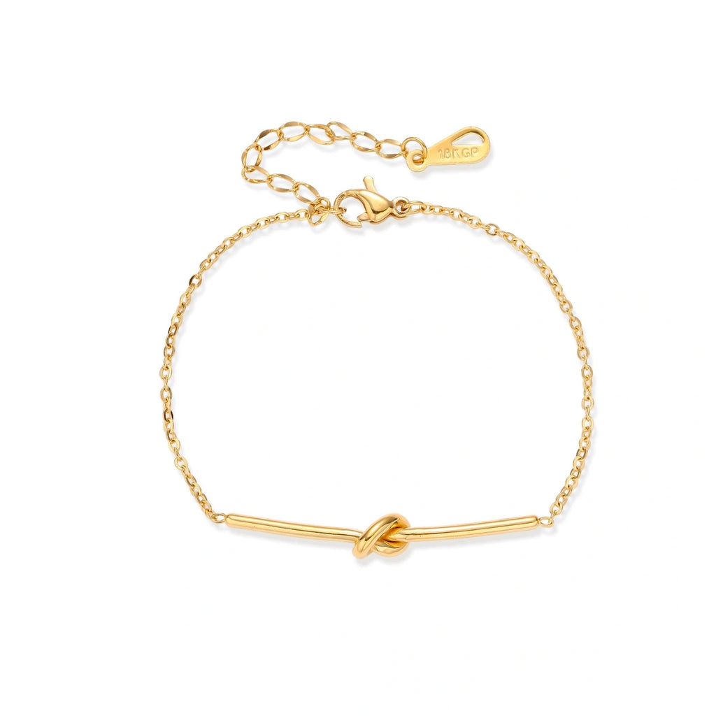 Delicate gold chain bracelet with minimalist bar and centered knot detail on cream background