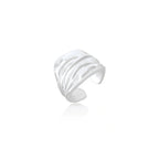 Wide sterling silver cuff ring with flowing wave patterns creating dimensional texture against cream background