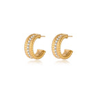 Textured gold huggie hoop earrings with raised ribbed rows creating dimensional sculptural design on cream background