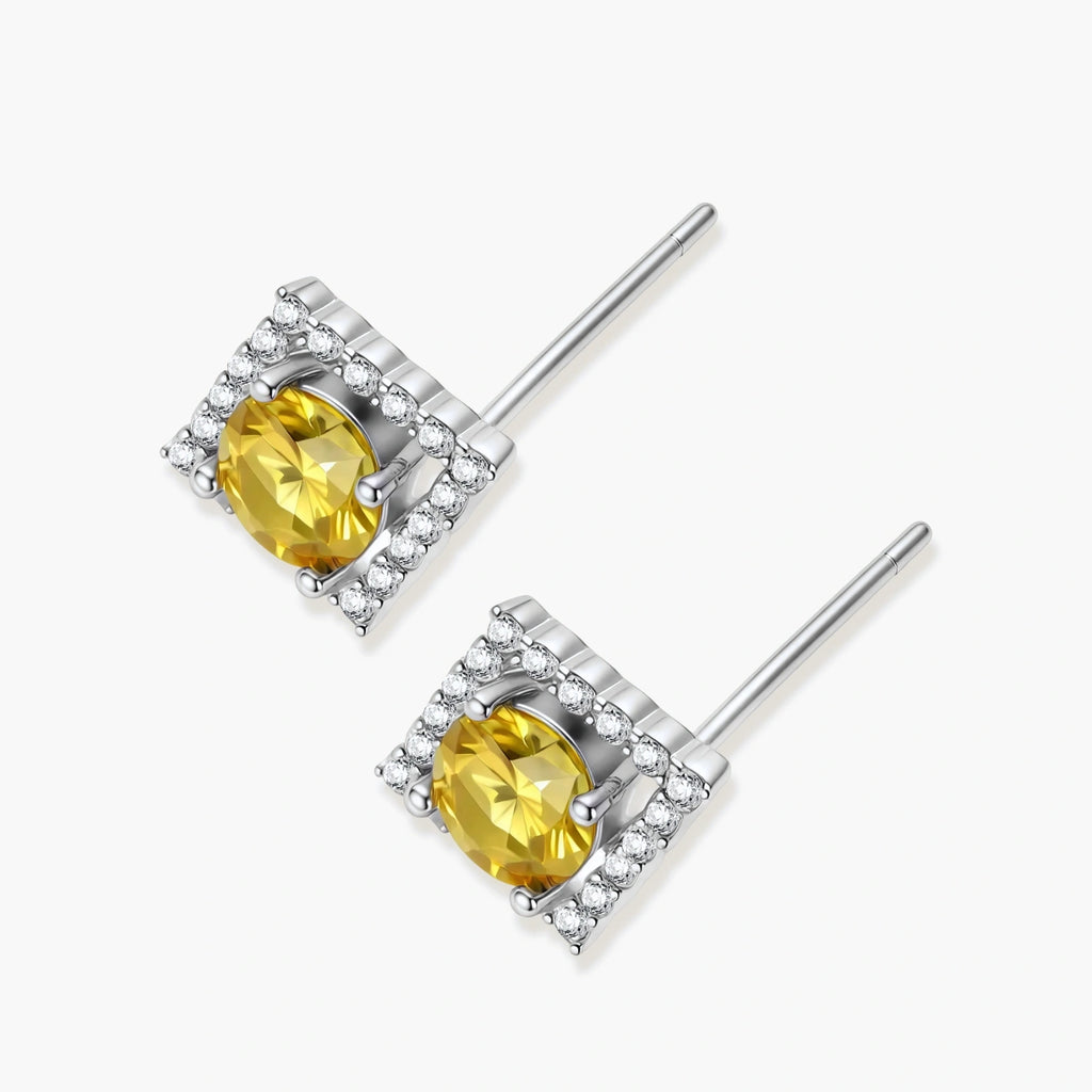 Close-up of diamond-shaped stud earrings with yellow moissanite centers and clear stone halos in sterling silver setting