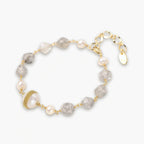 Bracelet with cloudy quartz beads, freshwater pearls, and gold-wrapped baroque pearl centerpiece on white background.