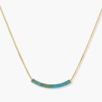 Gold-plated curved necklace and hoop earrings with turquoise cubic zirconia stones on white background.